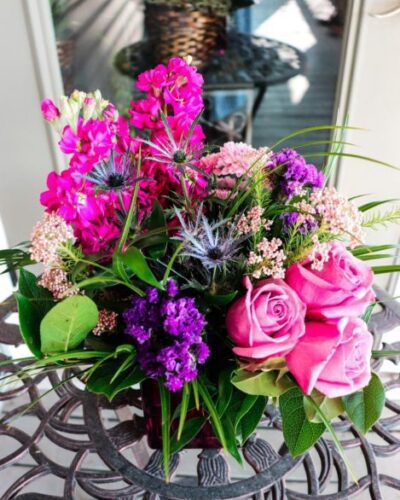 "Purple Rain" flower arrangement with lavender, pink, and blue blooms in a pink glass cube vase.
